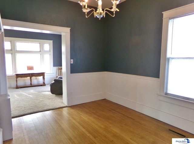 empty room with visible vents, wood finished floors, wainscoting, and a chandelier