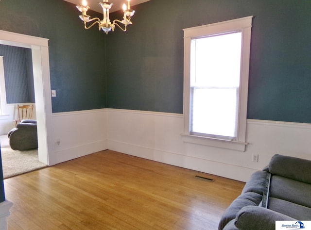 spare room featuring a wainscoted wall, a notable chandelier, visible vents, and wood finished floors