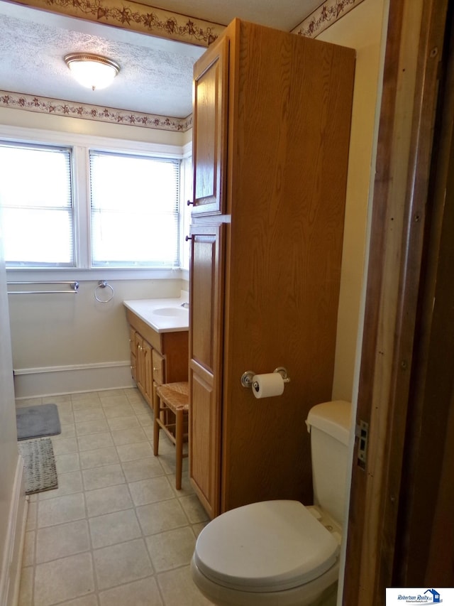 bathroom with baseboards, toilet, vanity, tile patterned floors, and a textured ceiling