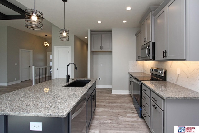 kitchen with pendant lighting, appliances with stainless steel finishes, sink, light stone counters, and a center island with sink