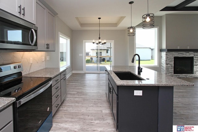 kitchen with a center island with sink, appliances with stainless steel finishes, a raised ceiling, decorative light fixtures, and sink