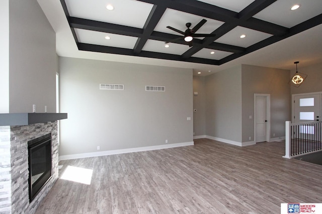 unfurnished living room featuring ceiling fan, beam ceiling, wood-type flooring, coffered ceiling, and a stone fireplace