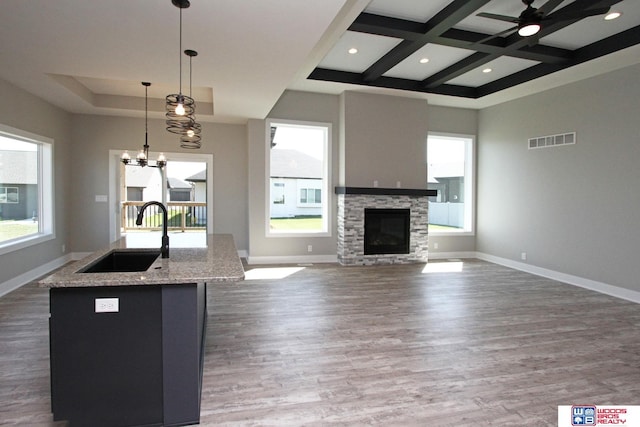 kitchen featuring a center island with sink, sink, coffered ceiling, hanging light fixtures, and dark wood-type flooring