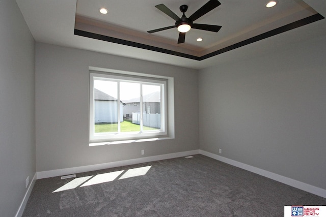 empty room with ceiling fan, dark carpet, and a raised ceiling