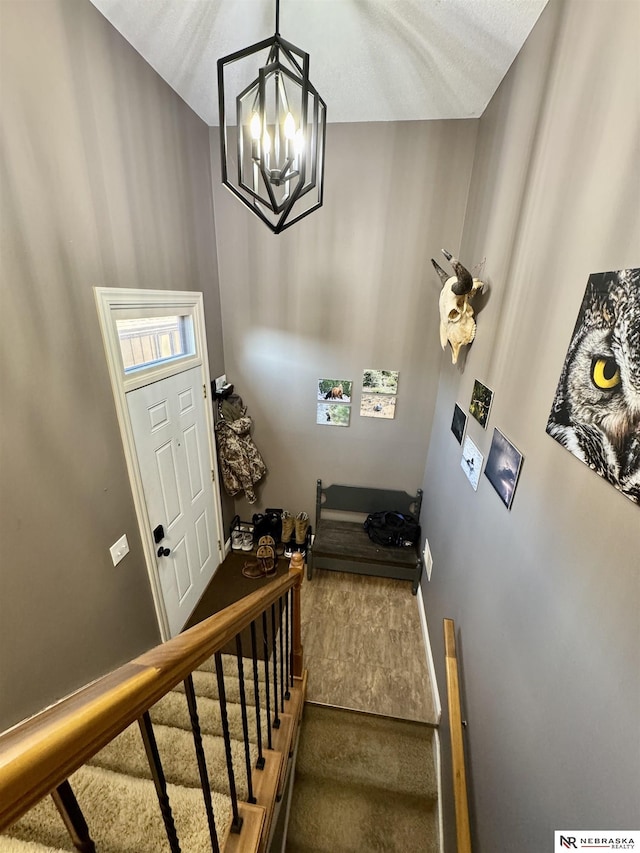 stairway featuring a textured ceiling, an inviting chandelier, and carpet floors