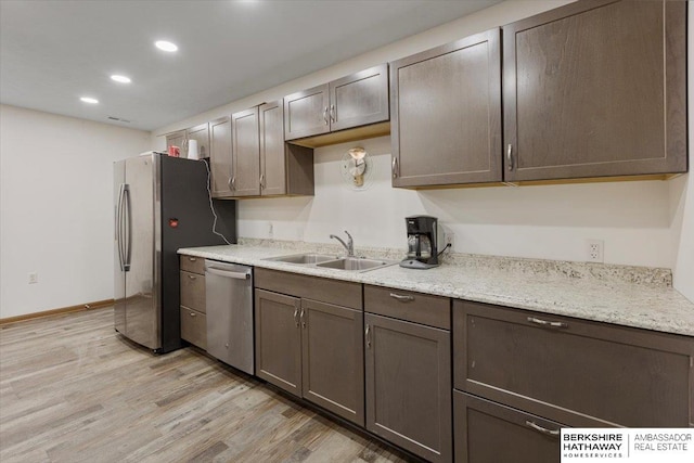 kitchen featuring sink, light stone counters, dark brown cabinets, appliances with stainless steel finishes, and light hardwood / wood-style floors