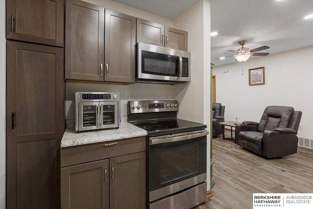 kitchen with appliances with stainless steel finishes, ceiling fan, dark brown cabinetry, light stone countertops, and light wood-type flooring