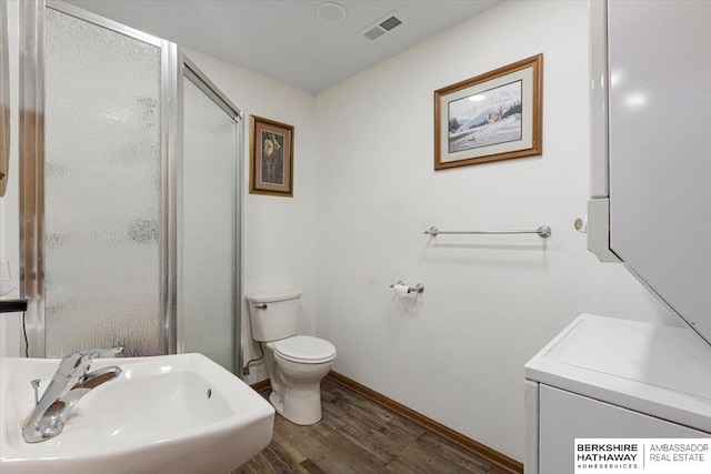 bathroom featuring sink, hardwood / wood-style floors, washer / clothes dryer, a shower with shower door, and toilet