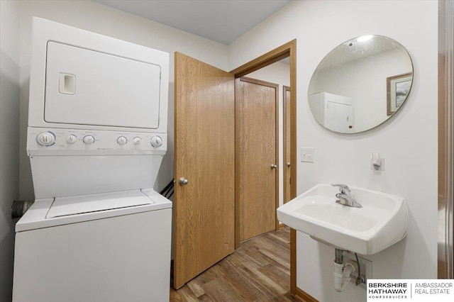 clothes washing area featuring stacked washer / drying machine, sink, and light hardwood / wood-style flooring