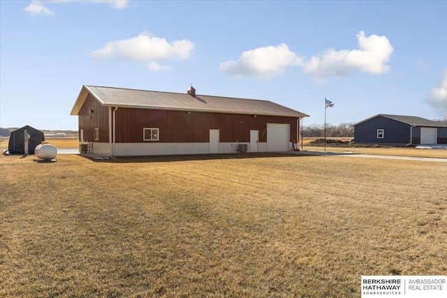 rear view of property with a garage, an outdoor structure, and a lawn