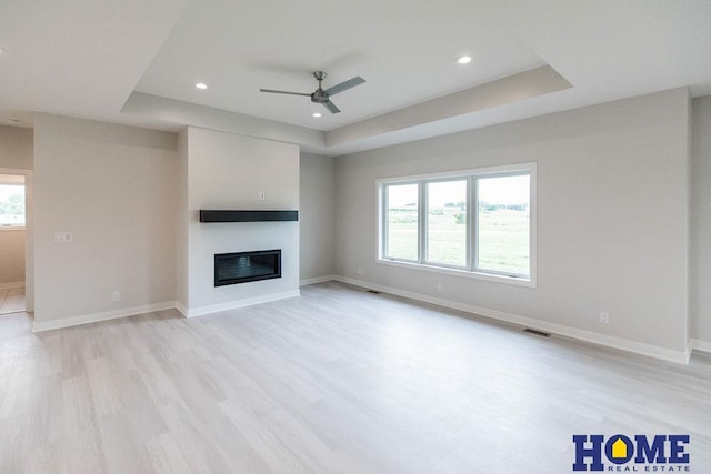 unfurnished living room featuring ceiling fan, light wood-type flooring, and a tray ceiling