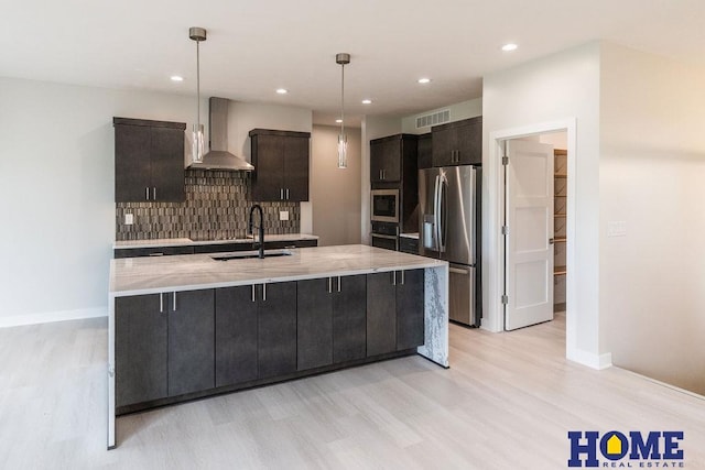 kitchen featuring appliances with stainless steel finishes, pendant lighting, wall chimney exhaust hood, light hardwood / wood-style flooring, and sink