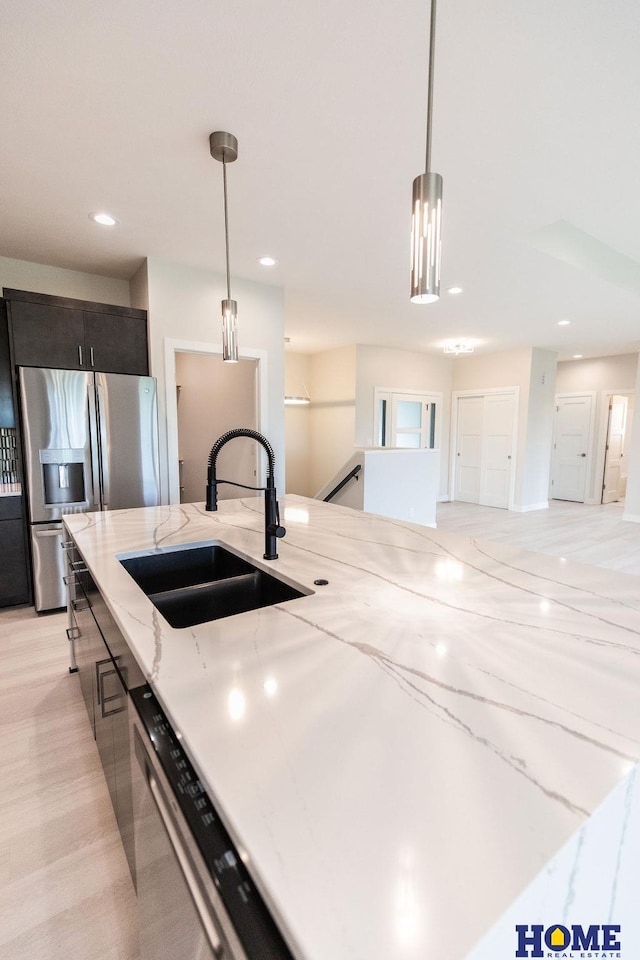 kitchen with light stone countertops, pendant lighting, dark brown cabinetry, sink, and stainless steel fridge