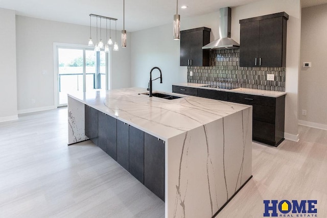 kitchen with tasteful backsplash, wall chimney range hood, a spacious island, pendant lighting, and sink