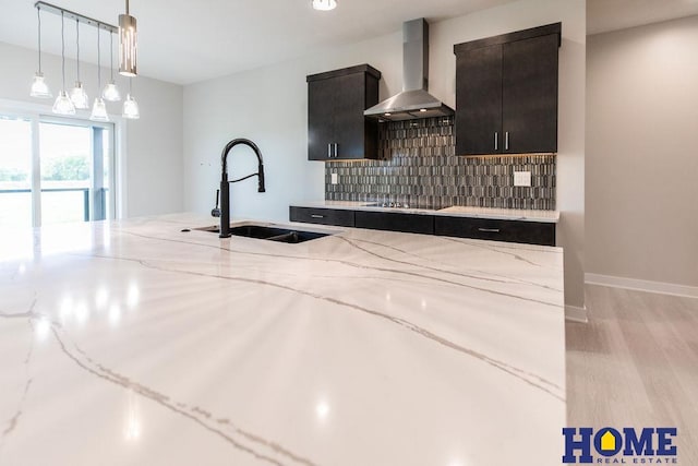 kitchen featuring wall chimney range hood, decorative backsplash, sink, light stone counters, and black electric cooktop