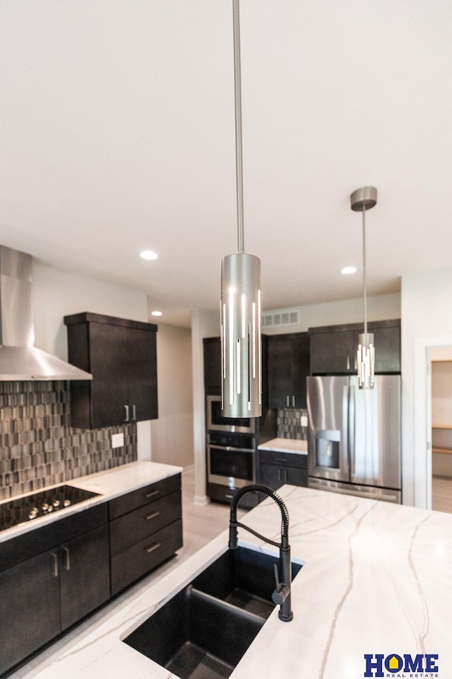 kitchen featuring decorative light fixtures, sink, wall chimney range hood, and stainless steel appliances