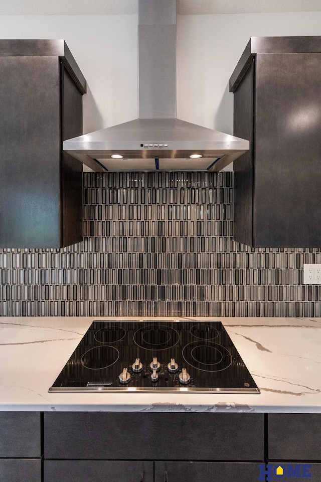 kitchen featuring tasteful backsplash, light stone countertops, wall chimney exhaust hood, and black electric cooktop