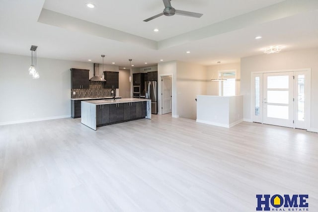 kitchen with stainless steel refrigerator with ice dispenser, light hardwood / wood-style flooring, a center island with sink, and wall chimney range hood