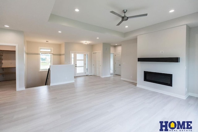 unfurnished living room with light wood-type flooring, ceiling fan, and a raised ceiling