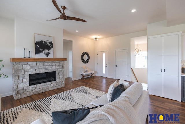 living room with ceiling fan, dark wood-type flooring, and a stone fireplace