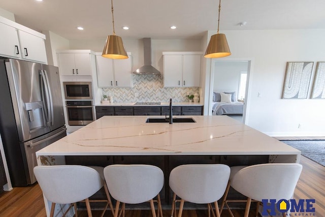 kitchen featuring white cabinetry, appliances with stainless steel finishes, wall chimney exhaust hood, and hanging light fixtures