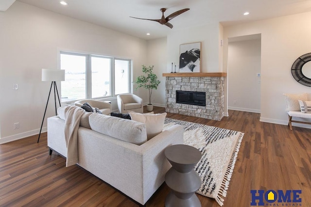 living room featuring ceiling fan, dark wood-type flooring, and a stone fireplace