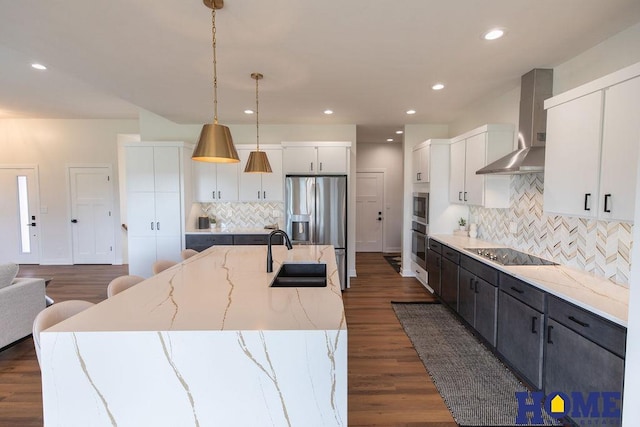 kitchen featuring white cabinetry, stainless steel appliances, hanging light fixtures, wall chimney exhaust hood, and sink