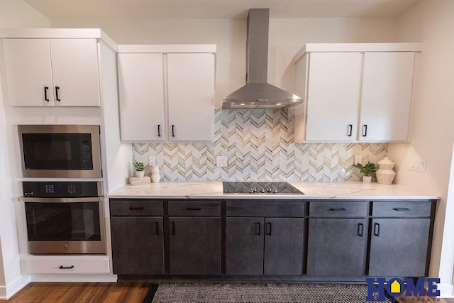 kitchen with wall chimney range hood, white cabinetry, stainless steel oven, light stone countertops, and built in microwave