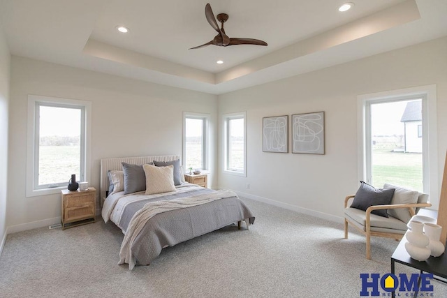 carpeted bedroom featuring ceiling fan, multiple windows, and a raised ceiling