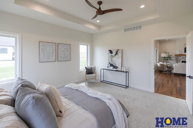 carpeted bedroom featuring ceiling fan, a fireplace, and a raised ceiling