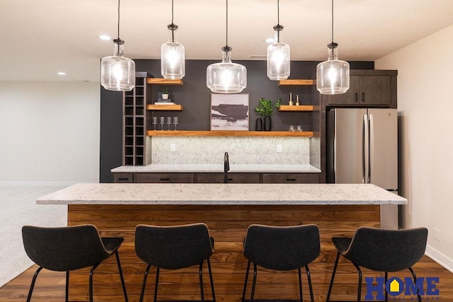 bar with light stone countertops, pendant lighting, sink, and stainless steel refrigerator