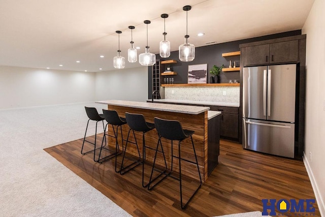 kitchen with dark brown cabinetry, a kitchen bar, hanging light fixtures, stainless steel refrigerator, and a center island with sink