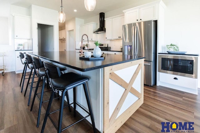 kitchen with built in microwave, stainless steel fridge, wall chimney exhaust hood, and white cabinetry