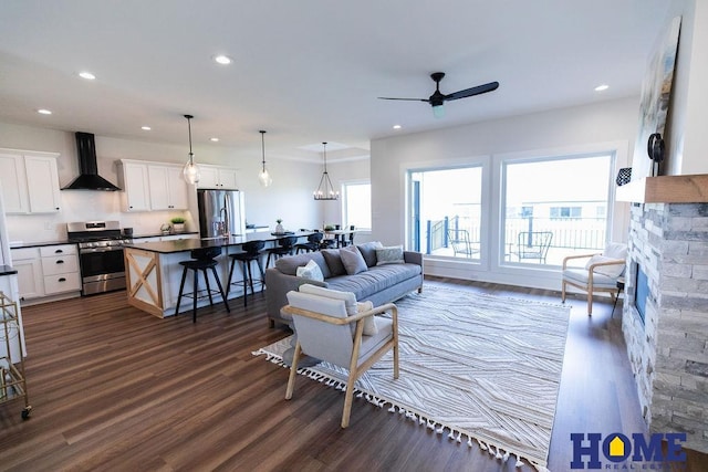 living room featuring ceiling fan, dark wood-type flooring, and a stone fireplace