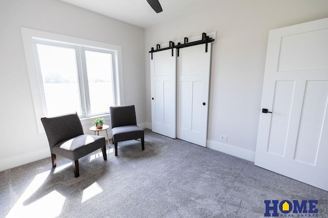 living area featuring carpet floors, a barn door, and ceiling fan