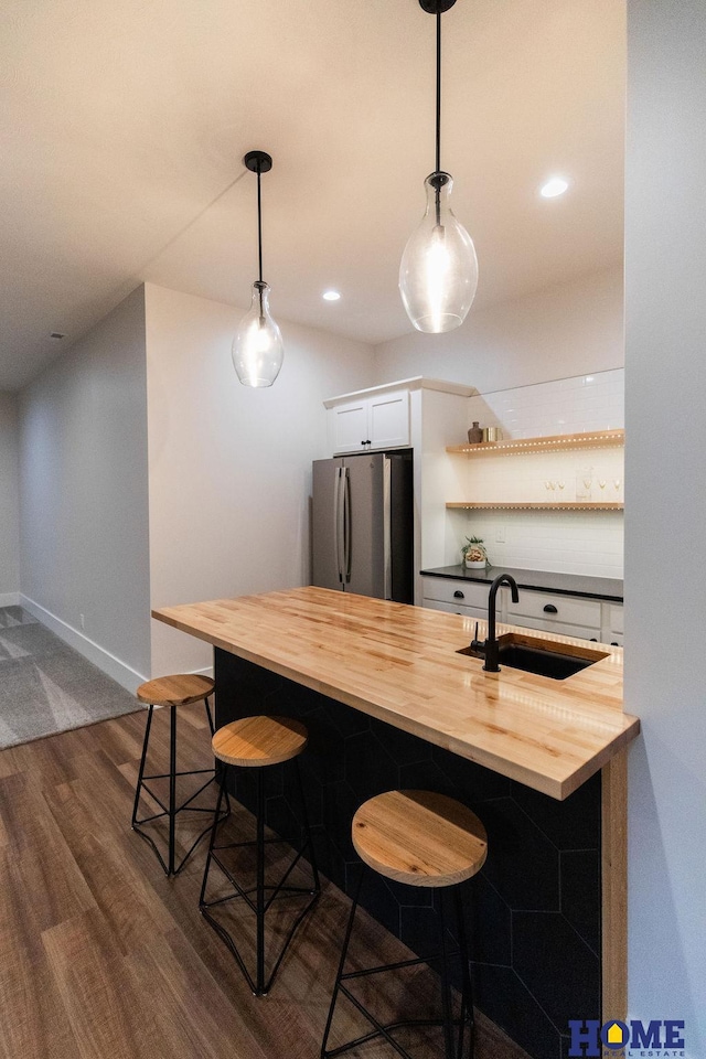 kitchen with white cabinetry, sink, stainless steel refrigerator, butcher block countertops, and a breakfast bar area