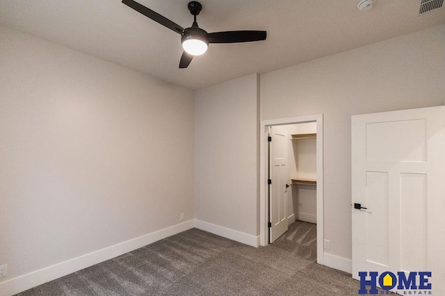 unfurnished bedroom featuring ceiling fan, a closet, a walk in closet, and dark colored carpet