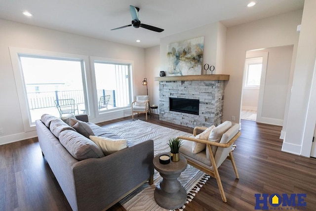 living room featuring dark wood-type flooring, a wealth of natural light, and a stone fireplace