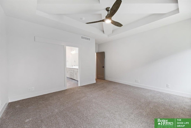 unfurnished bedroom featuring light carpet, ceiling fan, a tray ceiling, and ensuite bath