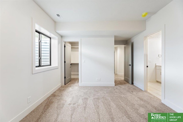 unfurnished bedroom with a spacious closet, ensuite bathroom, and light colored carpet