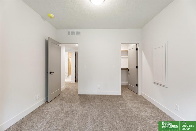 unfurnished bedroom with light colored carpet, a textured ceiling, and a walk in closet