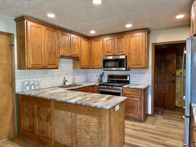 kitchen featuring light stone countertops, appliances with stainless steel finishes, sink, kitchen peninsula, and light wood-type flooring