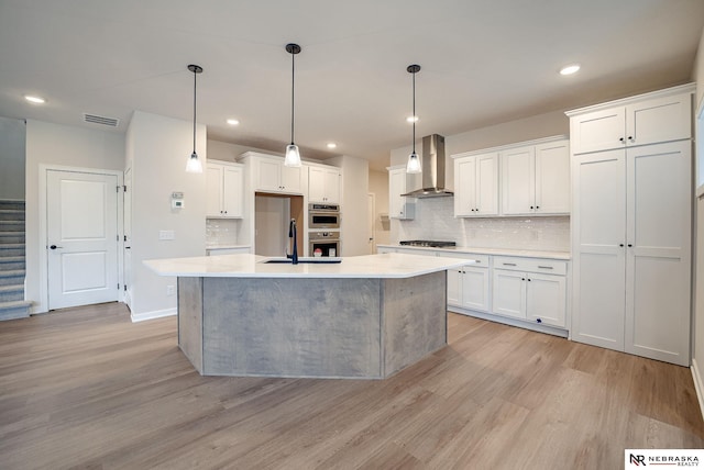 kitchen featuring white cabinetry, light hardwood / wood-style flooring, a center island with sink, and wall chimney range hood