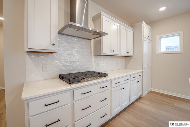 kitchen featuring white cabinetry, decorative backsplash, light wood-type flooring, stainless steel gas cooktop, and wall chimney exhaust hood