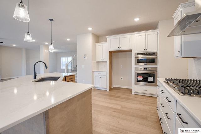 kitchen with decorative light fixtures, wall chimney range hood, sink, white cabinetry, and appliances with stainless steel finishes