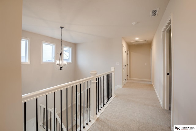 hallway with light colored carpet and a chandelier