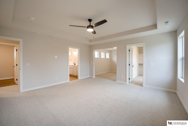 unfurnished bedroom featuring a spacious closet, ceiling fan, connected bathroom, a tray ceiling, and a closet