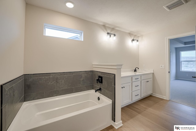 bathroom with wood-type flooring, a wealth of natural light, a bathtub, and vanity