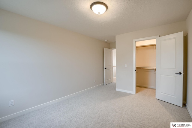 unfurnished bedroom with light carpet, a closet, a spacious closet, and a textured ceiling