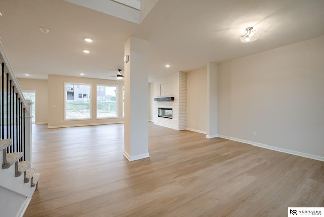 unfurnished living room with a brick fireplace, light hardwood / wood-style floors, and ceiling fan